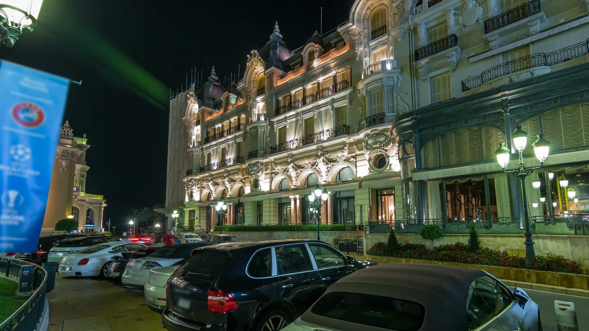 A row of cars are parked in front of a large building at night.