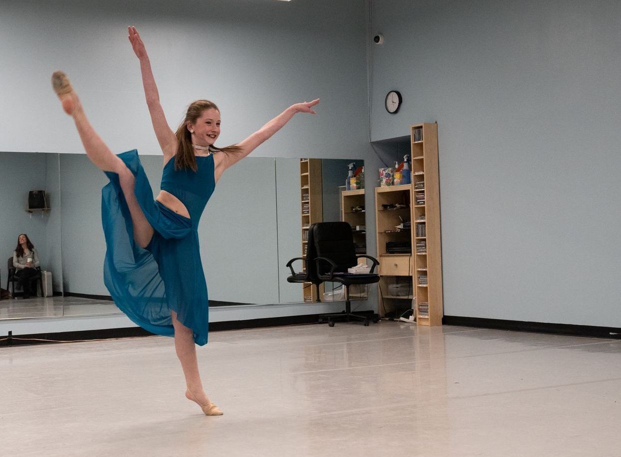 A woman in a blue dress is dancing in a dance studio.