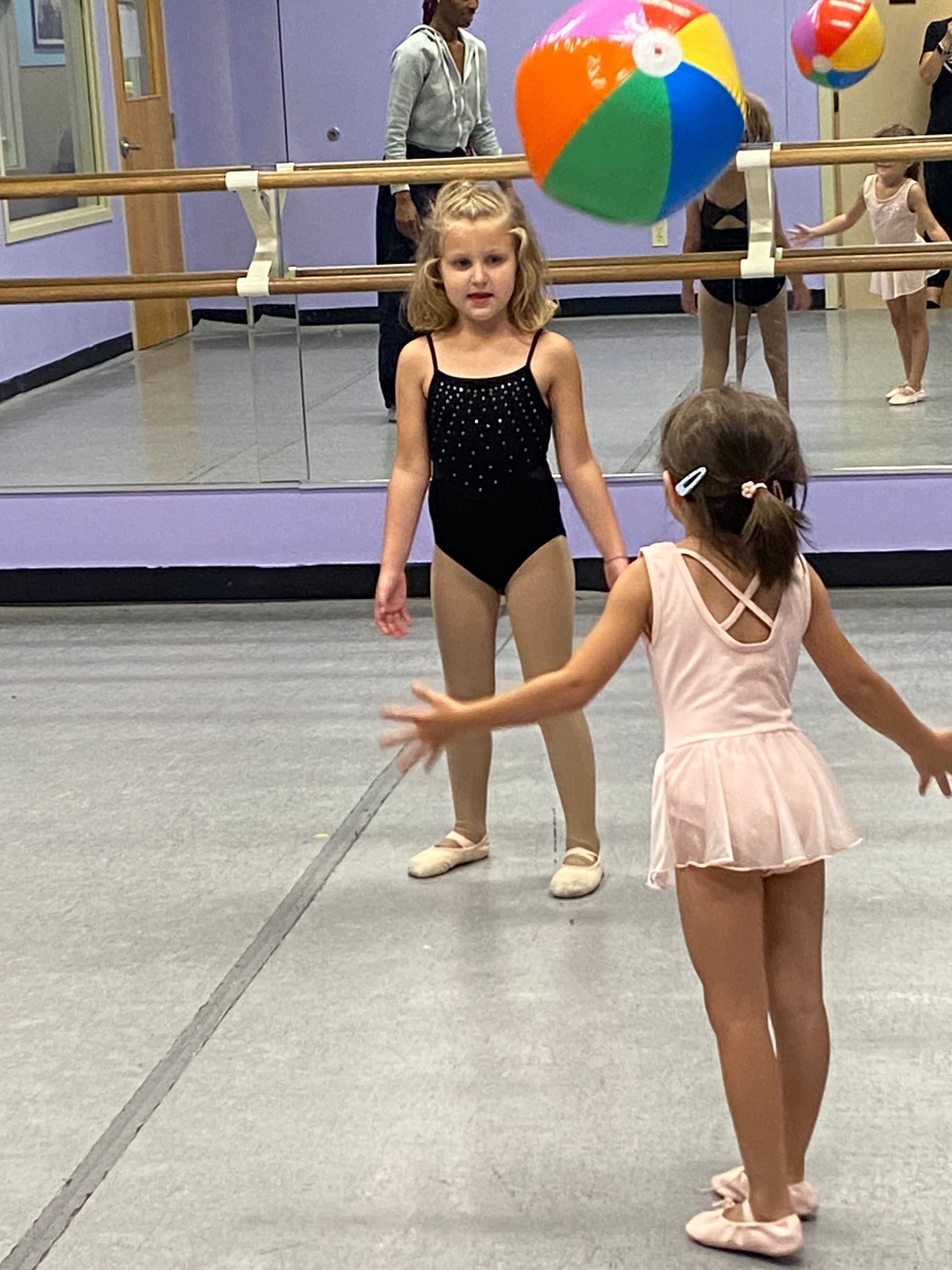 Two little girls are playing with a beach ball in a dance studio