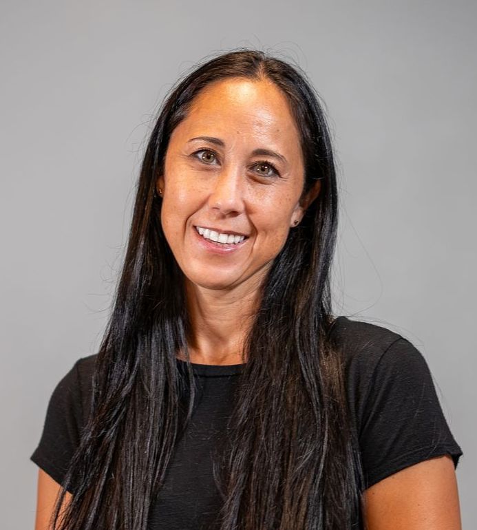 A woman with long dark hair is wearing a black shirt and smiling.