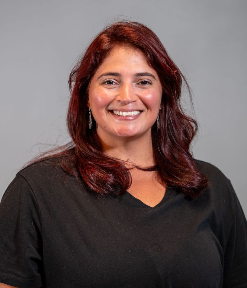 A woman with red hair is wearing a black shirt and smiling.