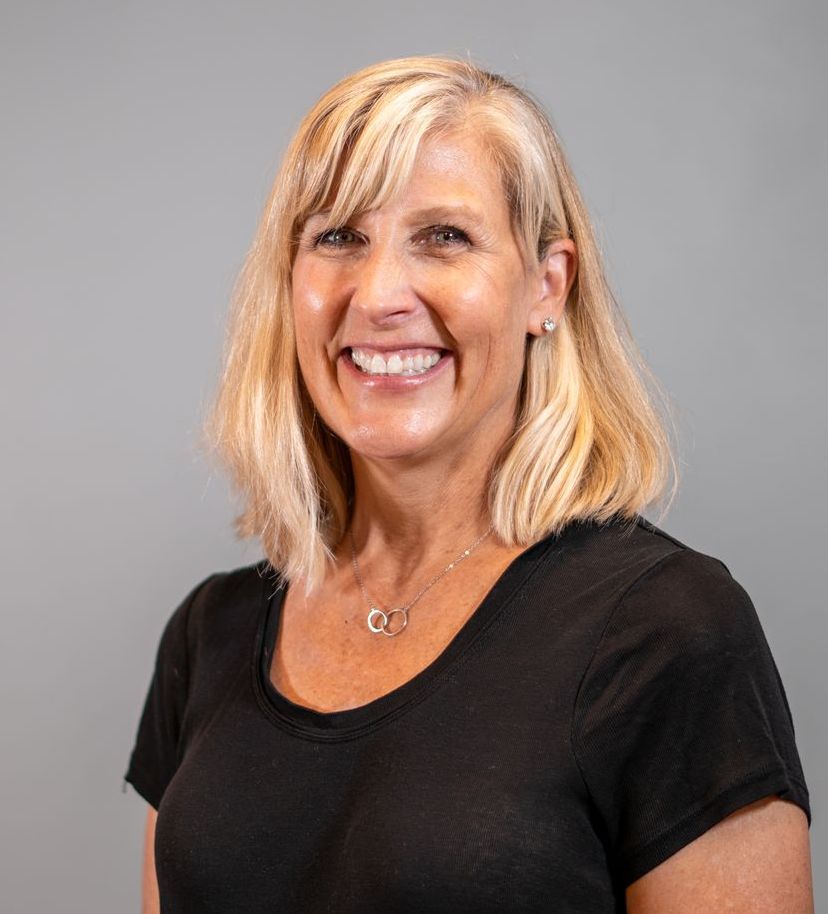 A woman wearing a black shirt and a necklace is smiling for the camera.