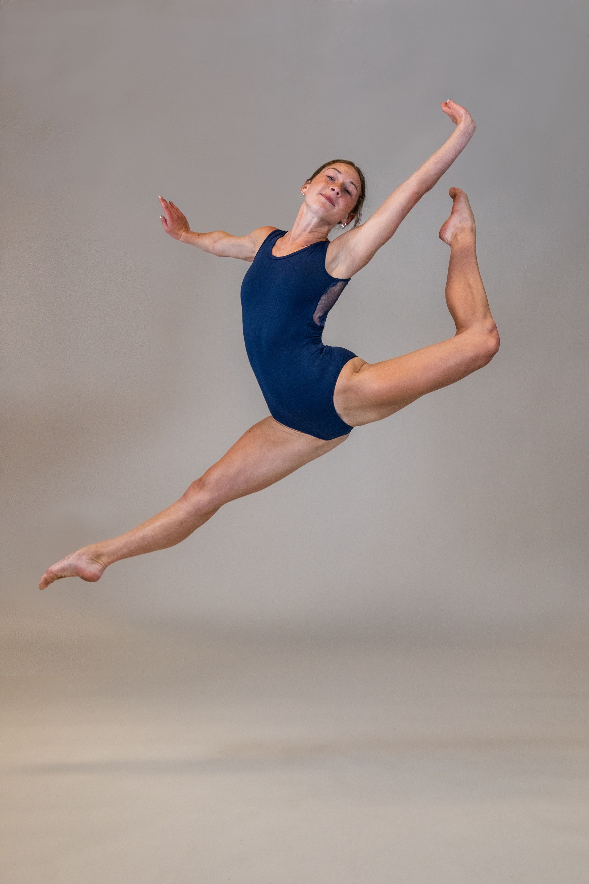 A young woman in a blue leotard is jumping in the air.