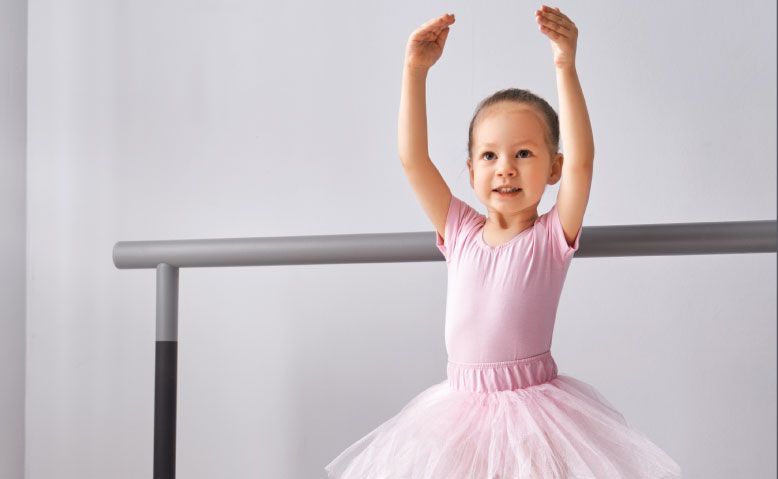 A little girl in a pink tutu is standing on a ballet barre.