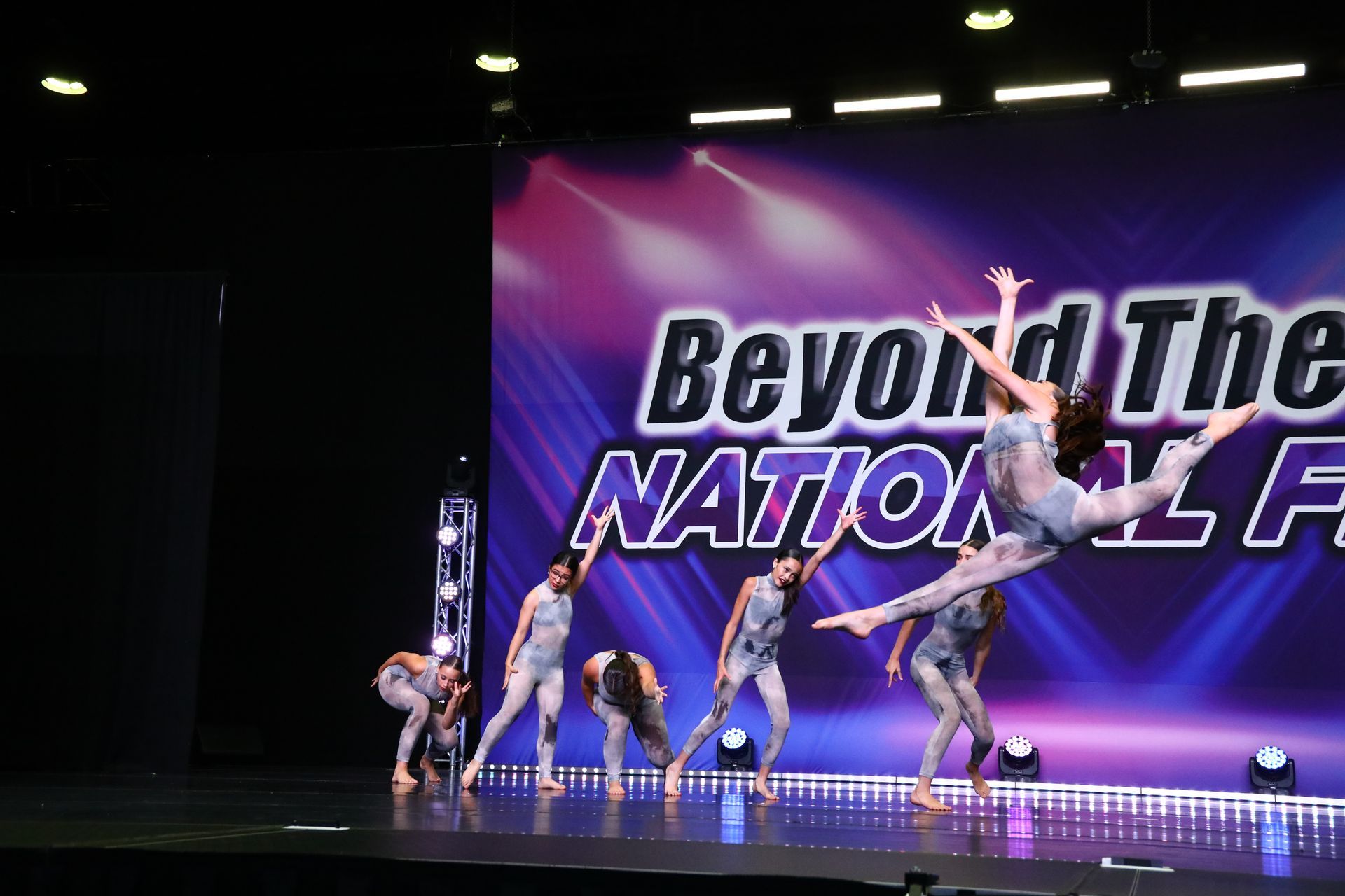 A group of dancers are performing on a stage in front of a sign that says beyond the nation.