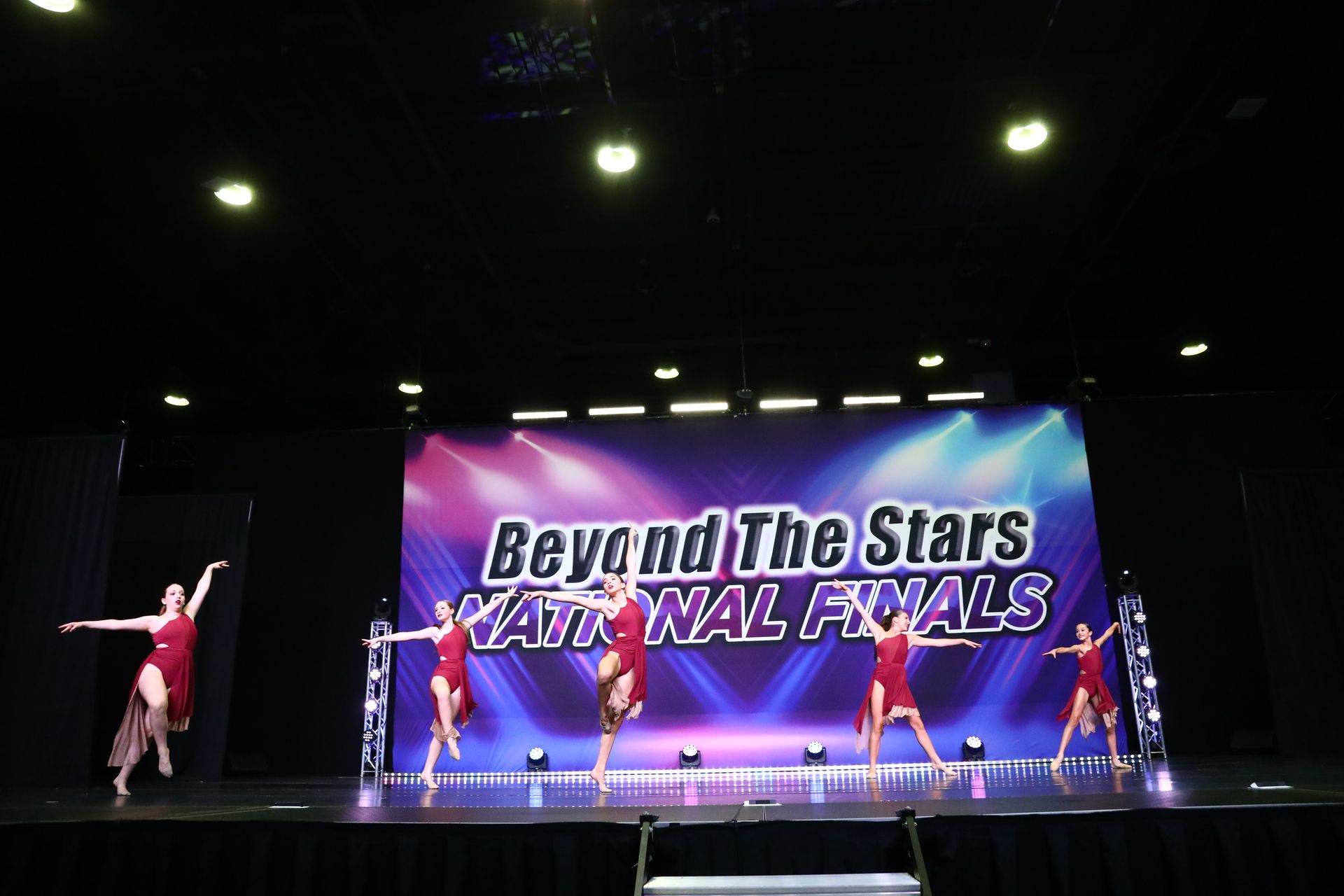 A group of dancers are performing on a stage in front of a large screen that says beyond the stars national finals