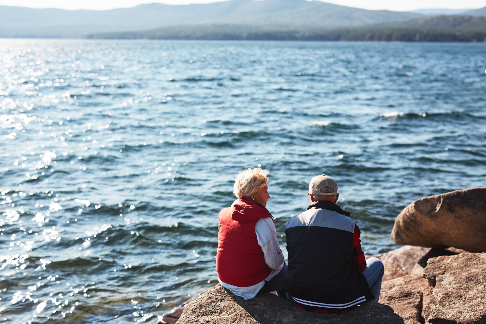 Graduate in cap and gown embraces another person holding diploma, smiling outside a building.