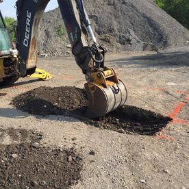 Une excavatrice creuse le sol sur un chantier. On aperçoit de la terre sombre.