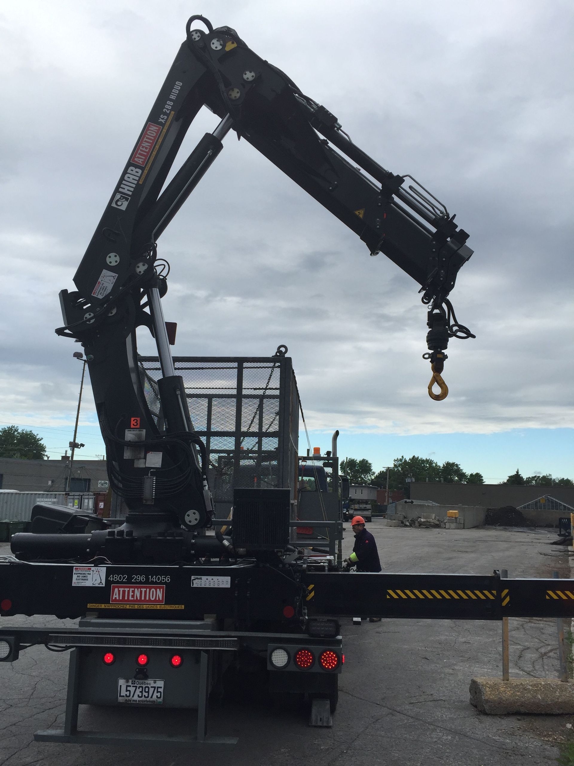 Grue noire montée sur un camion plateau ; une personne se tient à proximité, en extérieur.