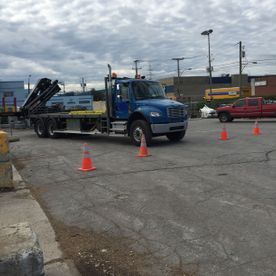 Camion bleu à plateau sur un parking, cônes de signalisation orange présents.