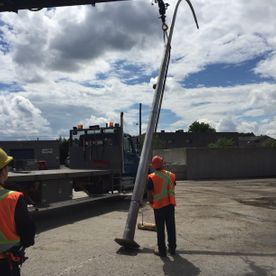 Deux ouvriers guident une longue perche métallique argentée suspendue à une grue de camion.