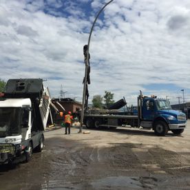 Des ouvriers chargent un lampadaire tordu sur un camion plateau par temps nuageux.