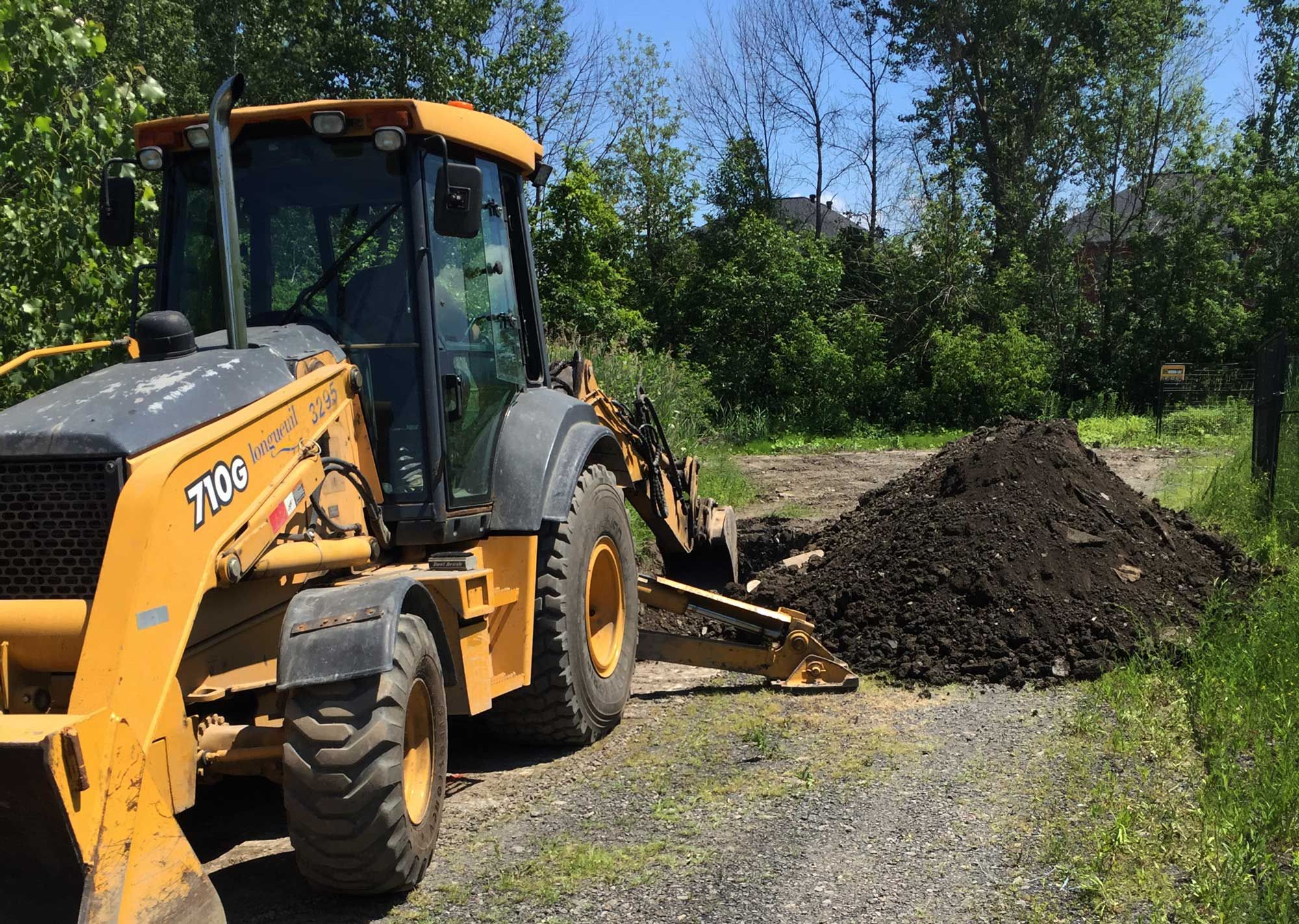 Une pelleteuse Case jaune à côté d'un tas de terre sur un chemin de gravier, avec des arbres en arrière-plan.
