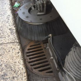 Les brosses d'une balayeuse de rue nettoient près d'un trottoir et d'une bouche d'égout.