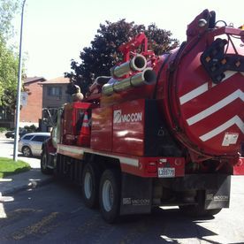 Un camion Vac-Con rouge est stationné dans une rue, probablement pour des travaux d'entretien des égouts ou des canalisations.