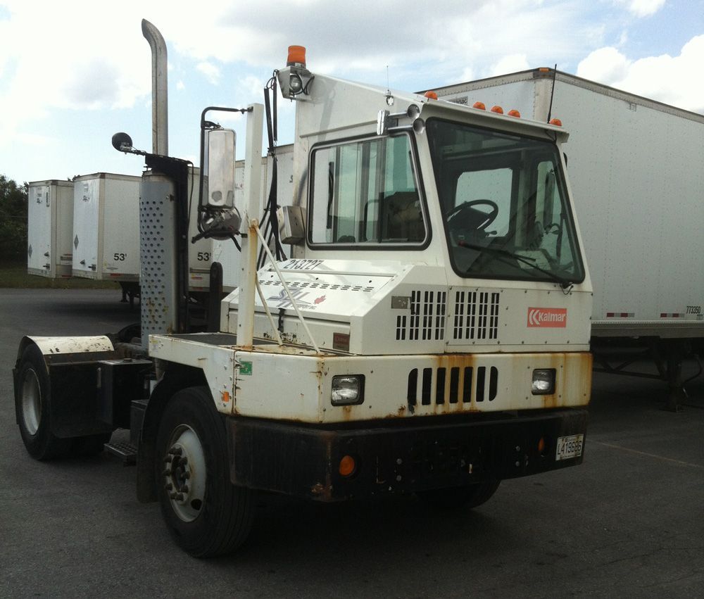 Un camion blanc avec une pile de remorques attelées, stationné à l'extérieur.