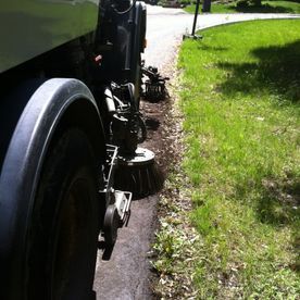 Une balayeuse nettoie le bord d'une route longeant une pelouse.