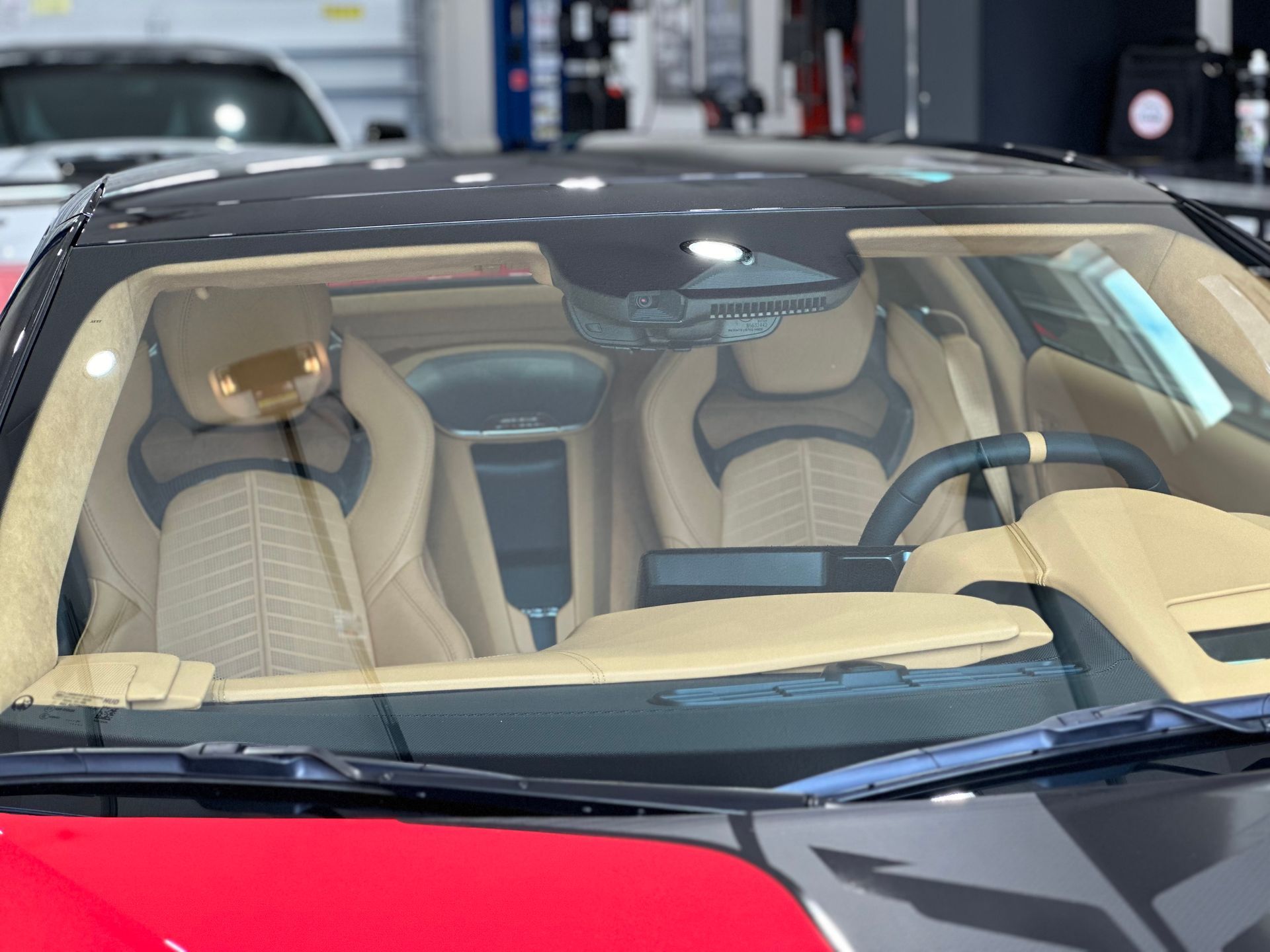 Interior of a red and black sports car showing tan leather seats and dashboard, a black steering wheel, and the windshield.