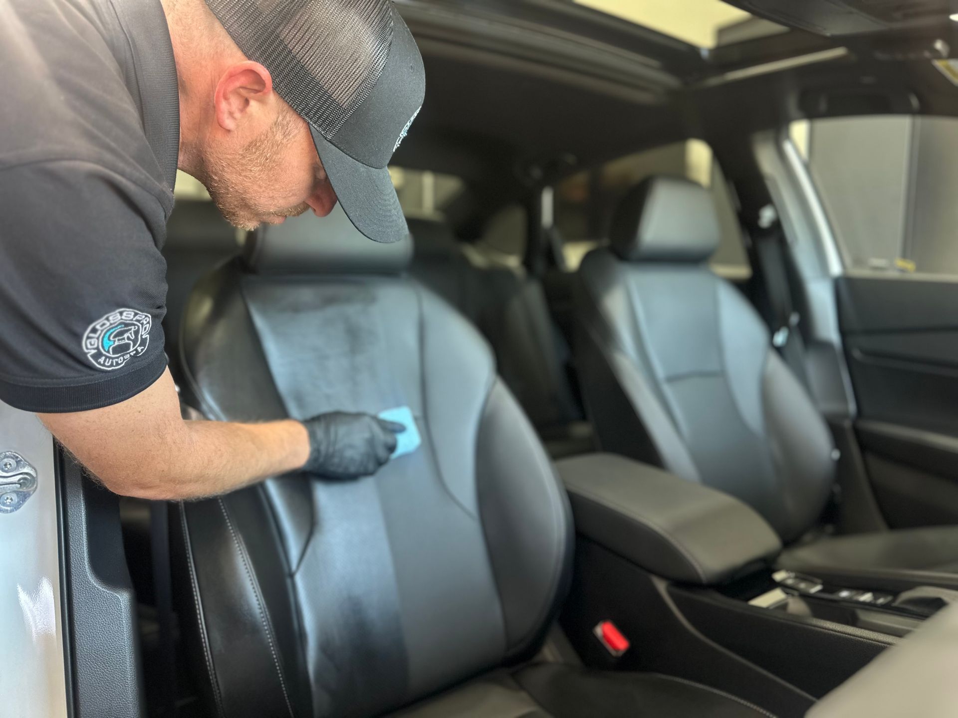 A person wearing black gloves cleans a black leather car seat.