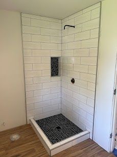 A shower stall with white tiles and a black tile floor in a bathroom.
