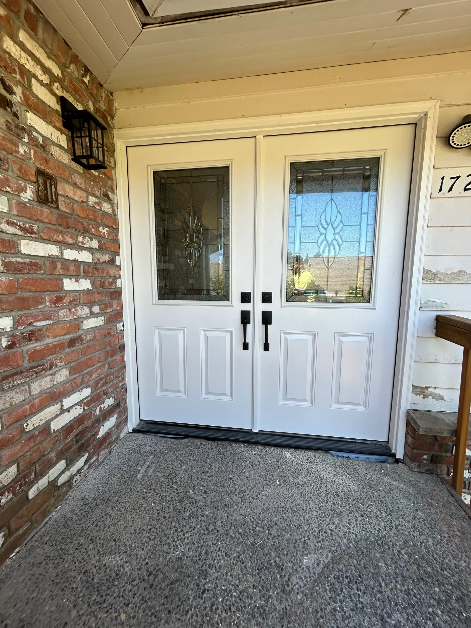 A white double door with a brick wall behind it.