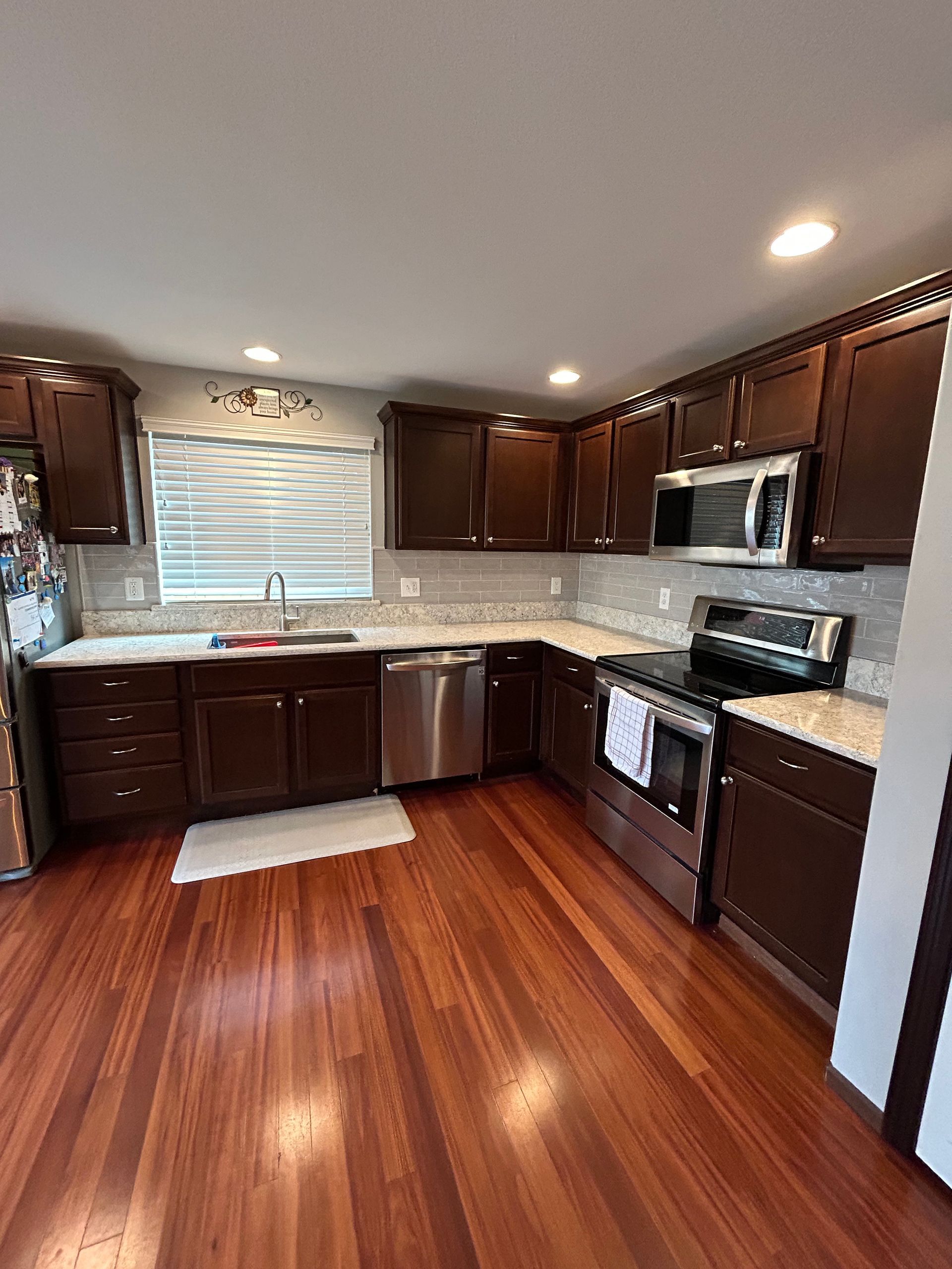A kitchen with hardwood floors , stainless steel appliances , and brown cabinets.
