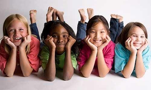 Four children smiling, lying on their stomachs, heads in hands.