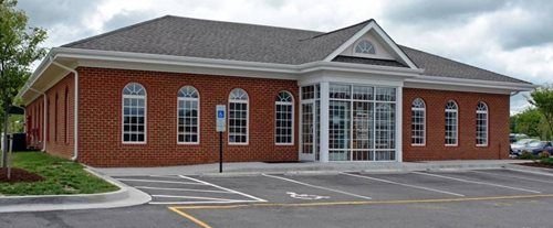 Brick building with arched windows, glass front entrance, and parking area.
