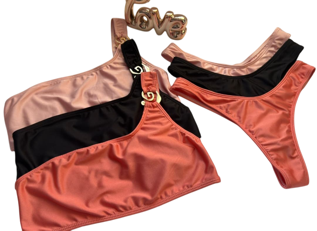 Trajes de baño apilados: tops de un solo hombro en tonos melocotón, negro y coral, y braguitas de tanga a juego. Herrajes dorados. Detalle 