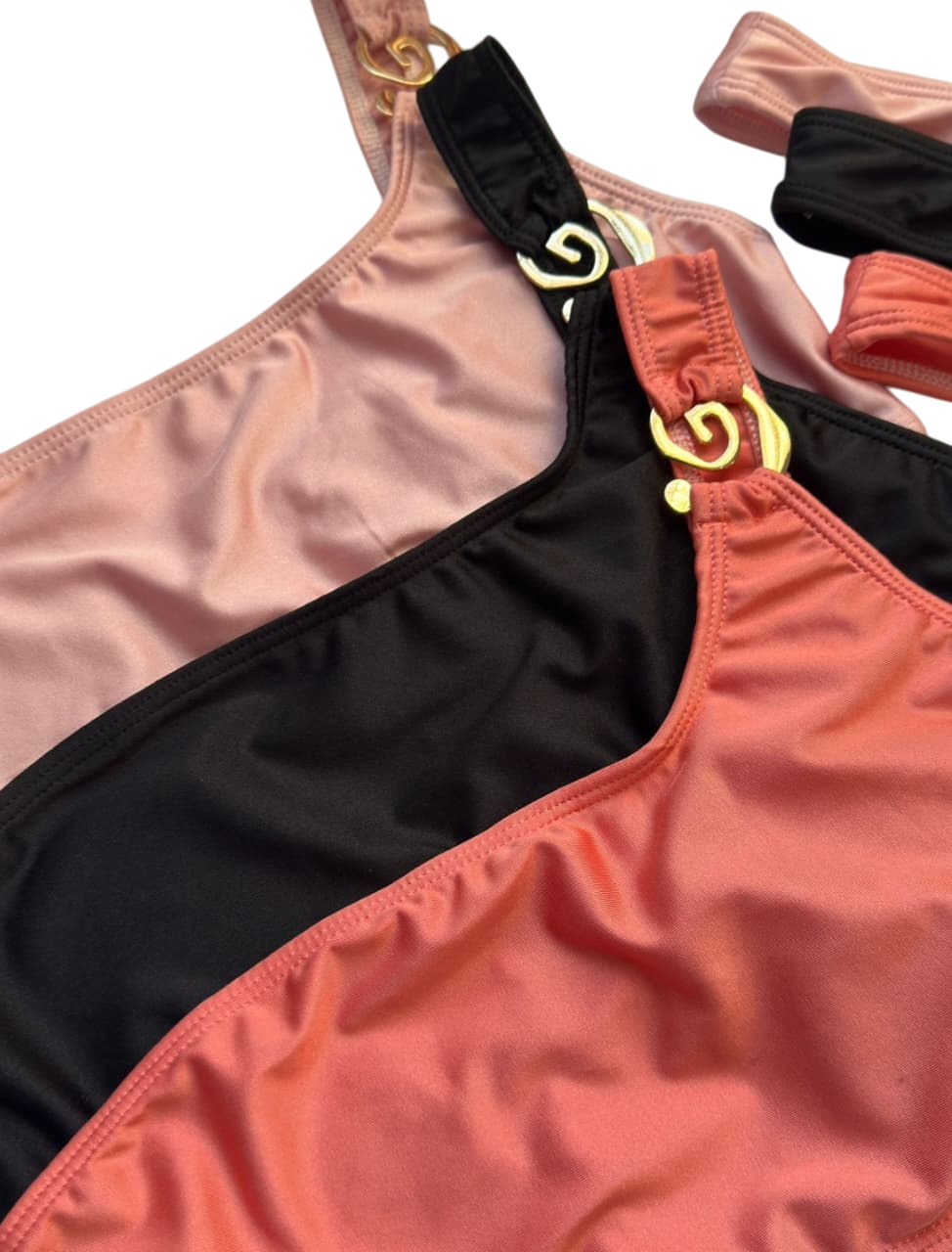 Tres tops de un solo hombro en rosa, negro y coral, con detalles de cadena dorada en los tirantes.