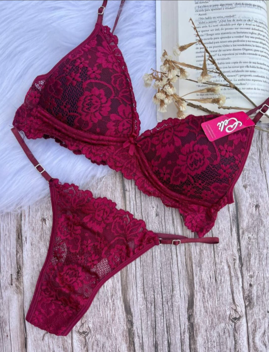 Conjunto de lencería de encaje burdeos: sujetador y tanga sobre una superficie de madera con un libro y flores.