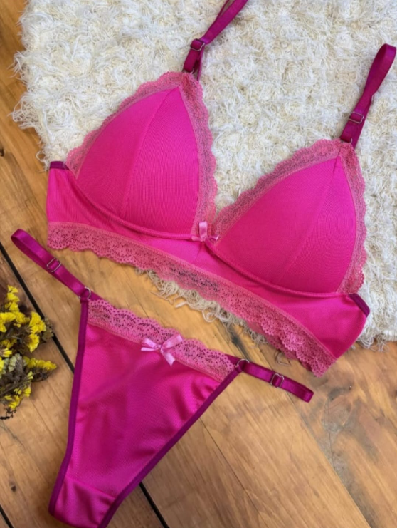 Conjunto de lencería rosa: sujetador y tanga con ribete de encaje, sobre alfombra blanca mullida y superficie de madera.