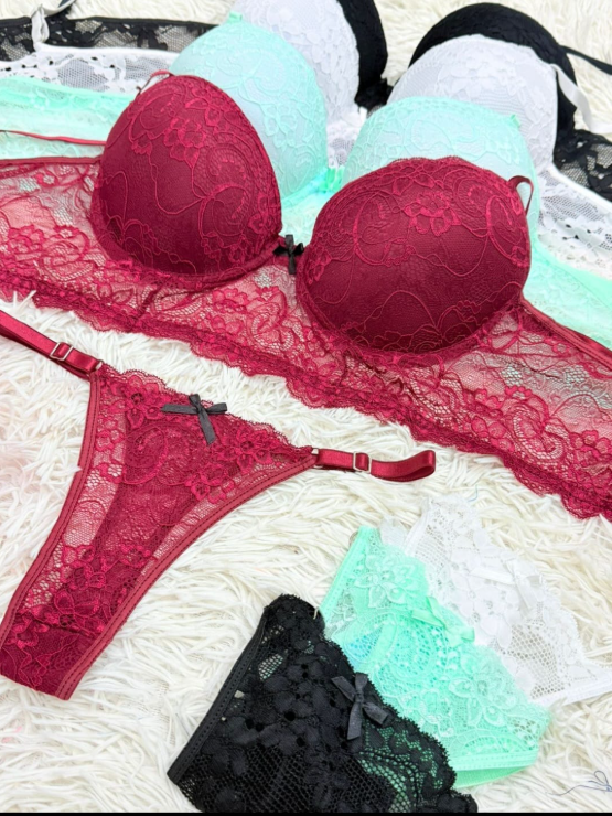 Conjunto de lencería: sujetador y tanga de encaje burdeos, con otros sujetadores en menta, negro y blanco. Caja Celie rosa.