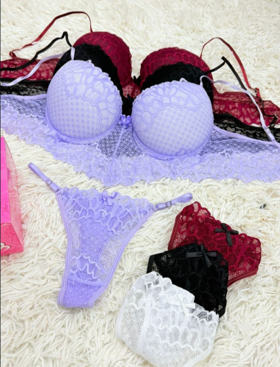 Conjunto de lencería: sujetador y tanga de encaje morado, bragas de encaje negro, rojo y blanco sobre una superficie blanca esponjosa.