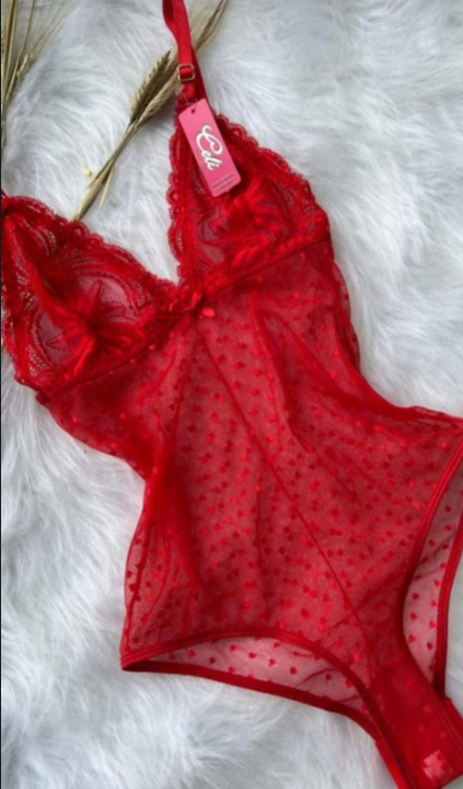 Lencería de encaje en tonos melocotón, negro, rojo y blanco, con tirantes finos, apilados sobre tela blanca arrugada.