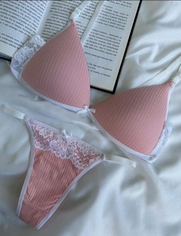 Conjunto de lencería de canalé rosa con ribete de encaje sobre sábana blanca, con un libro de fondo.