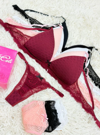 Conjunto de lencería: sujetador y tanga color burdeos, con otros sujetadores en color blanco, negro y rosa, sobre una superficie blanca esponjosa.