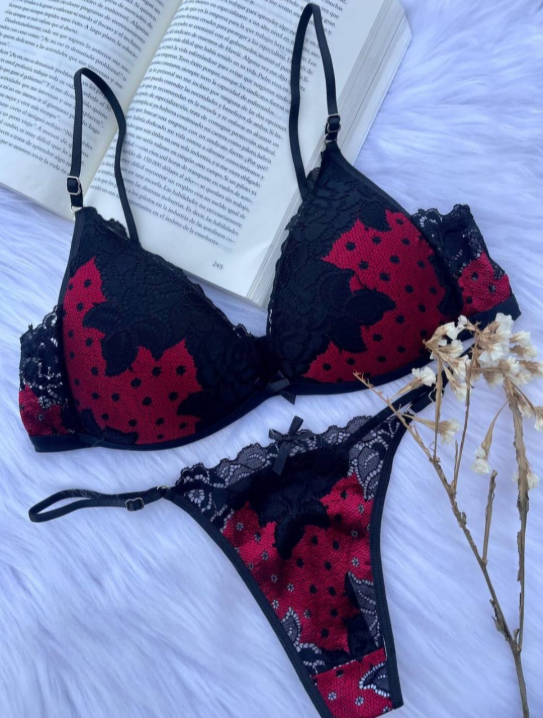 Conjunto de lencería negra y roja sobre superficie de piel blanca con libro abierto y flores secas.
