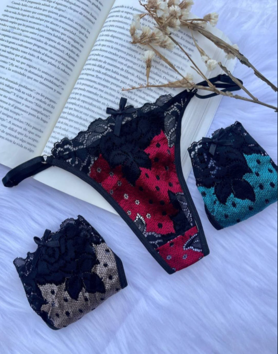 Conjunto de lencería negra y roja sobre superficie de piel blanca con libro abierto y flores secas.