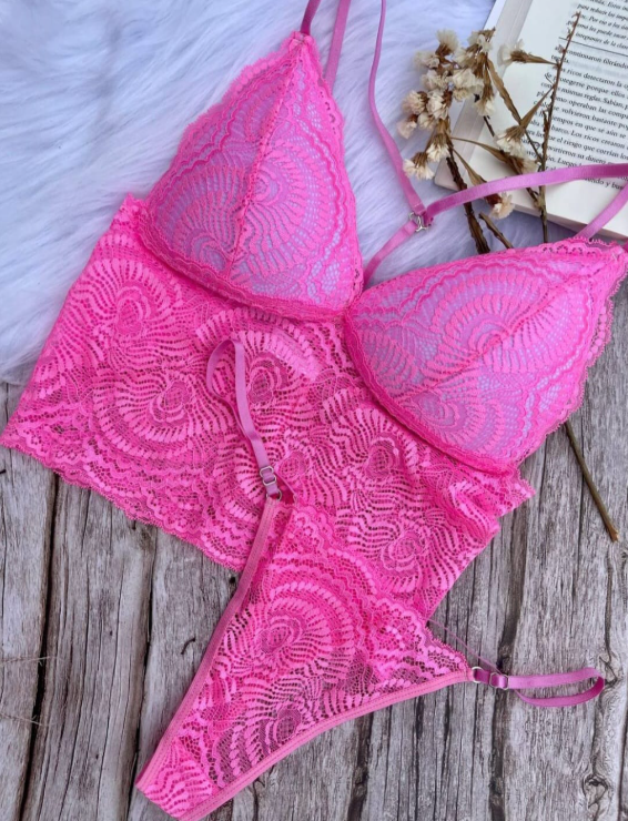 Conjunto de lencería de encaje rosa sobre superficie de madera, con un libro y flores de fondo.