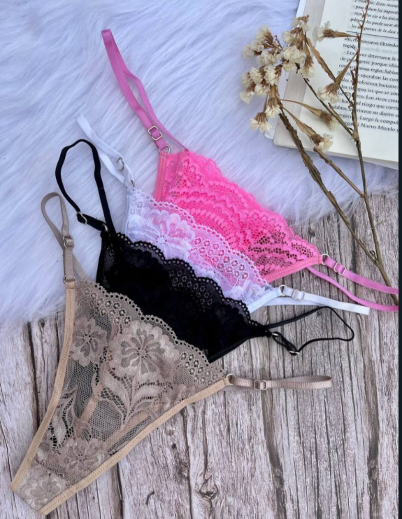 Conjunto de lencería de encaje rosa sobre superficie de madera, con un libro y flores de fondo.