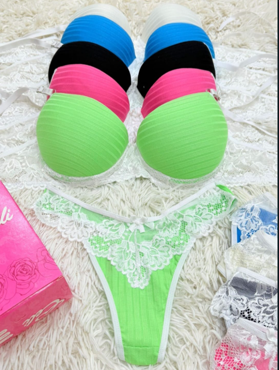 Colección de coloridos sujetadores sin tirantes y un tanga verde con ribete de encaje blanco sobre una superficie blanca esponjosa.