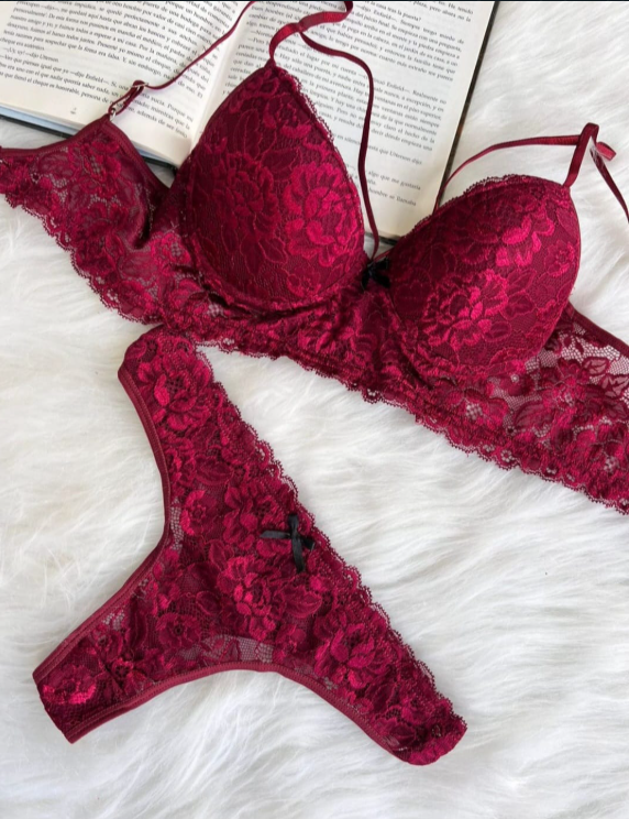 Mujer en lencería de encaje blanco, sentada en una cama, mirando hacia otro lado.