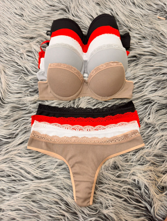 Pila de sujetadores coloridos y ropa interior a juego sobre una superficie gris peluda, con ribete de encaje.