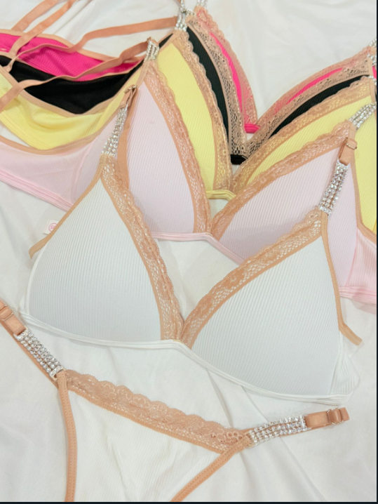 Primer plano de varios sujetadores triangulares coloridos con tirantes joya y ribete de encaje sobre tela blanca.