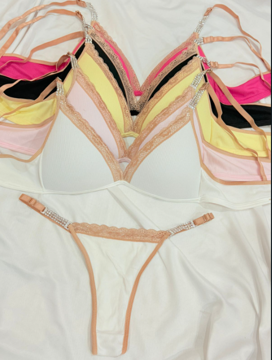 Primer plano de varios sujetadores triangulares coloridos con tirantes joya y ribete de encaje sobre tela blanca.