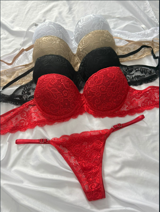 Conjunto de seis sujetadores de encaje y un tanga rojo a juego sobre una sábana blanca. Los sujetadores son de color blanco, beige, negro y rojo.