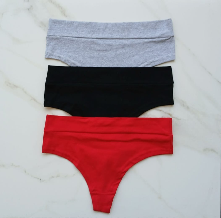 Tres prendas interiores estilo tanga: gris, negra y roja, apiladas sobre una superficie de mármol blanco.