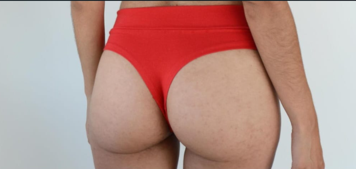 Tres prendas interiores estilo tanga: gris, negra y roja, apiladas sobre una superficie de mármol blanco.