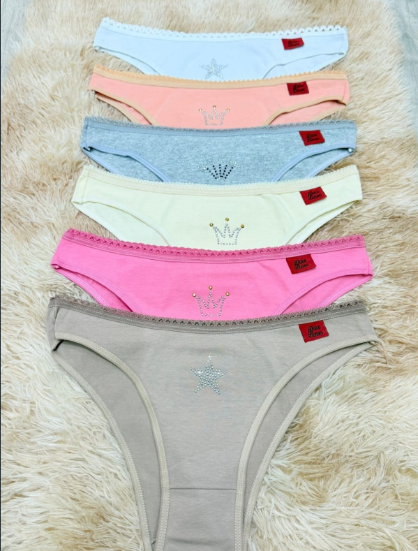 Seis pares de ropa interior femenina de colores sobre una alfombra mullida, cada uno con un detalle decorativo y una etiqueta roja.